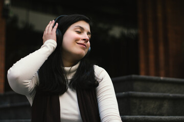Girl listening to music in the city. Women enjoying good music. Smiling girl with her eyes closed listening to music.