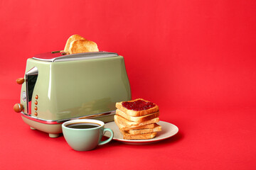 Bread slices in modern toaster, cup of coffee and tasty toasts with jam on red background
