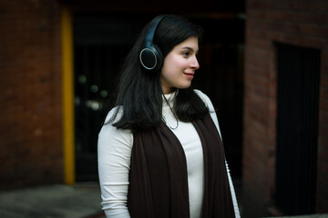 Smiling woman listening to music in the city. White woman with headphones listening to music. A woman looking into the distance