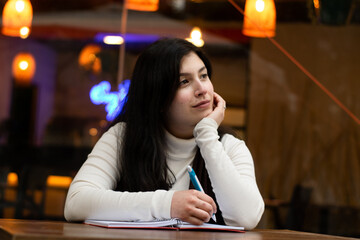 Seated woman writing. restaurant in the background. Thoughtful woman looking into the distance. Woman sitting outside a restaurant