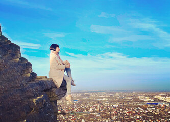 young woman sits on the edge of a cliff overlooking the city. City landscape on horizon. beautiful...