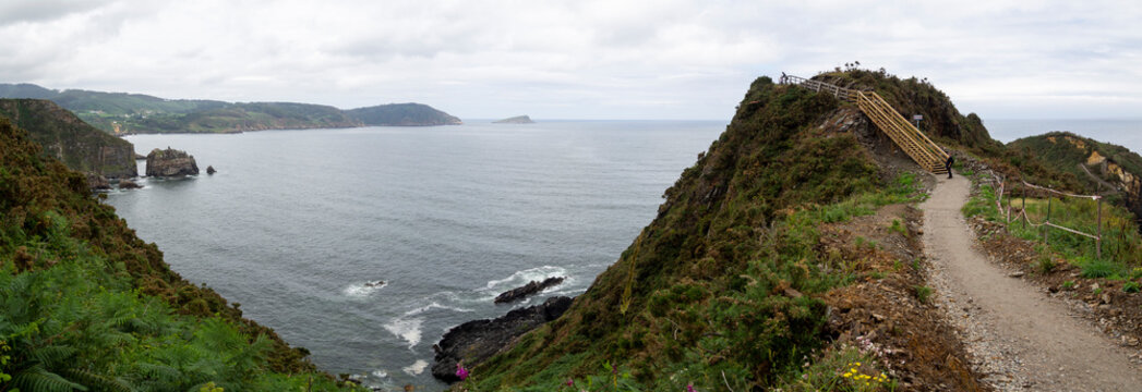 Vista panor&aacute;mica del mar y la costa gallega desde un camino de la punta de Foci&ntilde;o do Porco en Lugo, con agua azul, monta&ntilde;as verdes, islotes y acantilados en un d&iacute;a nuboso de verano de 2021