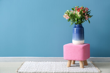 Vase with beautiful alstroemeria flowers on pouf near blue wall