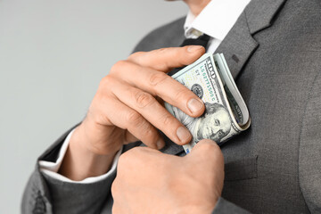 Businessman putting bribe in pocket on grey background, closeup