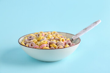 Bowl of colorful cereal rings with spoon on blue background