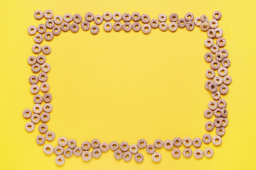 Frame made of grey cereal rings on yellow background