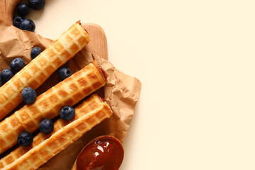 Delicious wafer rolls with boiled condensed milk and blueberries on beige background, closeup