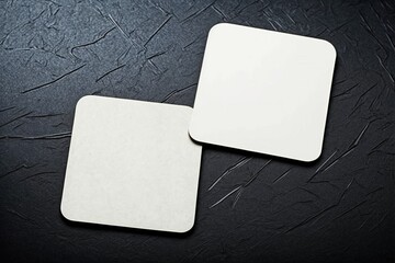 Two square beer coasters on black marble background