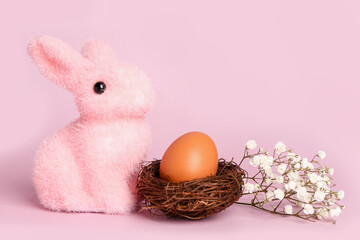 Nest with Easter egg, toy bunny and gypsophila flowers on pink background