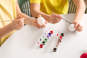 Little children painting Easter eggs at table in kitchen, closeup