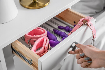 Woman opening drawer with sex toys in bedroom, closeup