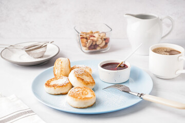 Plate with tasty cottage cheese pancakes, strawberry jam and cup of coffee on light background
