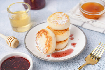 Plate with tasty cottage cheese pancakes, strawberry jam and honey on light background
