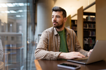 Fototapeta premium Portrait of attractive businessman, using laptop, hispanic man working online. Middle aged hipster guy working in modern office, looking away. Successful programmer sitting at desk