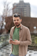 Obraz premium Smiling hispanic man using mobile phone, online communication standing on street