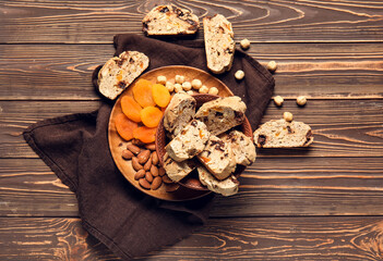 Board with delicious biscotti cookies, dried apricots and nuts on brown wooden background