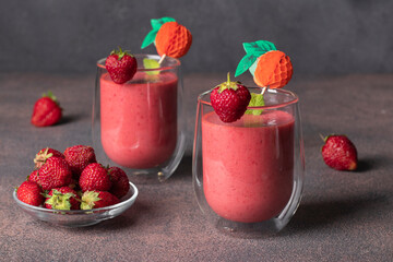 Strawberry smoothie of yogurt and ice cubes in two glass on brown table