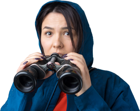 A tourist girl in a blue raincoat holds binoculars in her hands and looks into the distance, spies.