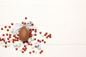 Candies and chocolate Easter egg tied with ribbon on white wooden background