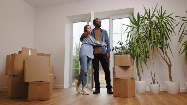 Happy african american man and caucasian woman moving to new home. Newly wed married couple shifting home. Man and woman holding each other and feel happy.