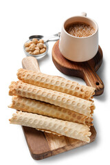 Board with delicious wafer rolls, hazelnuts and cup of coffee on grey background