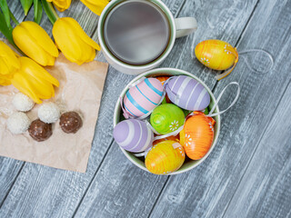 Easter eggs and tulips are on the table. View from above. Tea in a white cup and chocolates