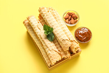 Board with delicious wafer rolls, boiled condensed milk and almond nuts on yellow background