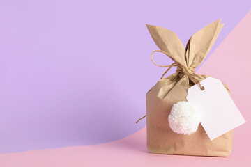 Easter bunny gift bag with blank tag on lilac and pink background