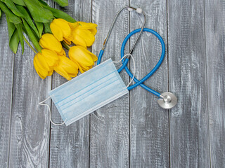 Yellow tulips, kn95 mask and stethoscope on a wooden background. Top view with copy space. Happy Nurse Day. Covid-19 concept. Vertical photo