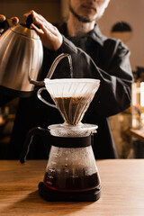 Pour over filter coffee alternative brewing method. Barista is pouring hot water over roasted and ground coffee beans contained in paper filter.