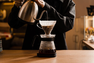 Drip filter coffee brewing. Barista pouring hot water over filter with ground coffee in the funnel. Pour over alternative method of pouring water over ground coffee beans contained in filter. - obrazy, fototapety, plakaty