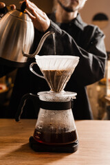 Pour over filter coffee alternative brewing method. Barista is pouring hot water over roasted and ground coffee beans contained in paper filter.