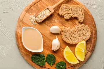 Fototapeta na wymiar Wooden board with bowl of tasty tahini, sesame seeds, bread, garlic and lemon slices on grunge background, closeup