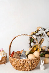 Basket with Easter eggs, bottle of wine and snacks on grey background
