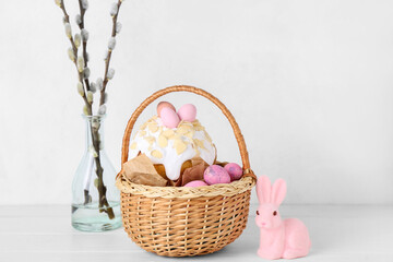 Basket with Easter eggs, cake, bunny and willow branches on white background
