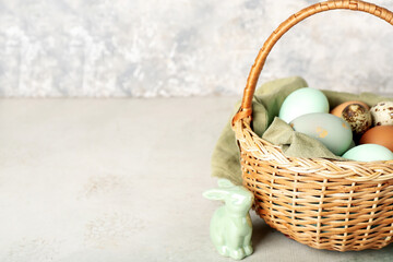 Basket with Easter eggs and bunny on table near grunge wall