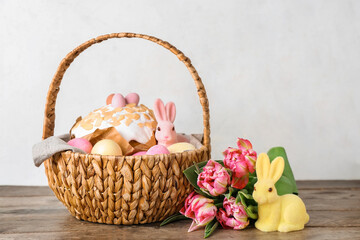 Basket with Easter eggs, cake, bunnies and tulip flowers on wooden table against grey background