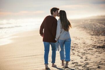 Beautiful young couple in love walking together in a cold winter day on the beach.