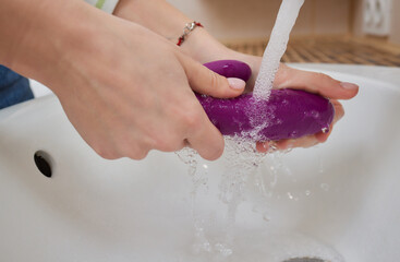 young woman washes a sex toy in the sink at home.
