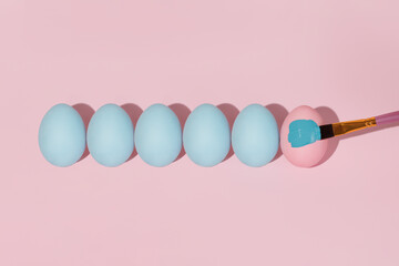 Pastel blue Easter eggs lie in a row isolated on a pink background. The brush paints the Easter egg blue. Traditional preparations for the Easter holiday.