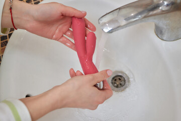 young woman washes a sex toy in the sink at home.