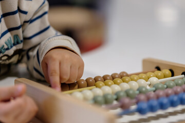Early development. Little kid toddler sitting at table with educational counting toy, playing with toys made from natural materials, child learning to count numbers in Montessori kindergarten
