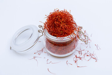 An overflowing glass jar of dry saffron stamens on a white table. Dry spice.