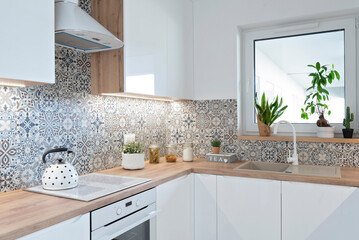 Modern design in stylish interior of kitchen with white furniture. Luxurious room with window and wooden counter with kettle. 