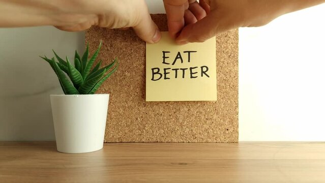 Paper note with text eat better on cork bulletin board. Healthy eating, dieting concept