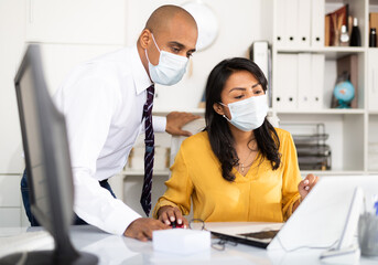Director in protective medical mask gives instructions to secretary in office