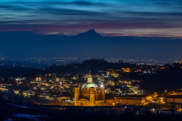 il profilo del monviso domina il santuario di vicoforte con la sua cupola ellittica,  illuminato dalle luci dopo il tramonto