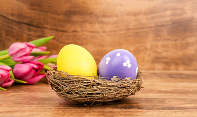 Two Easter eggs in a nest and tulips on wooden background