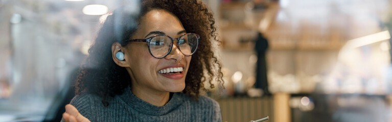 Smiling woman freelancer working laptop and talking phone while sitting near windows in cozy cafe