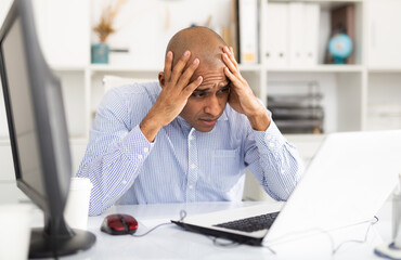 Frustrated tired office manager working at laptop